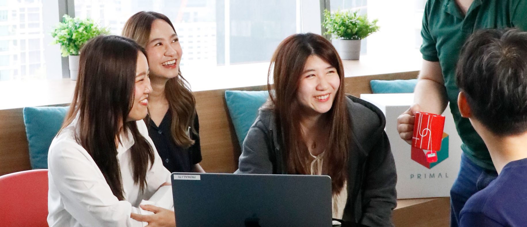 Four team members in a meeting looking at a laptop screen together in an office