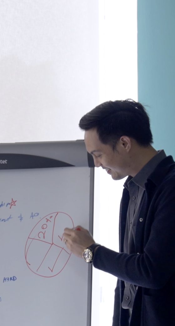 A man drawing a diagram in red marker on a whiteboard in a meeting room