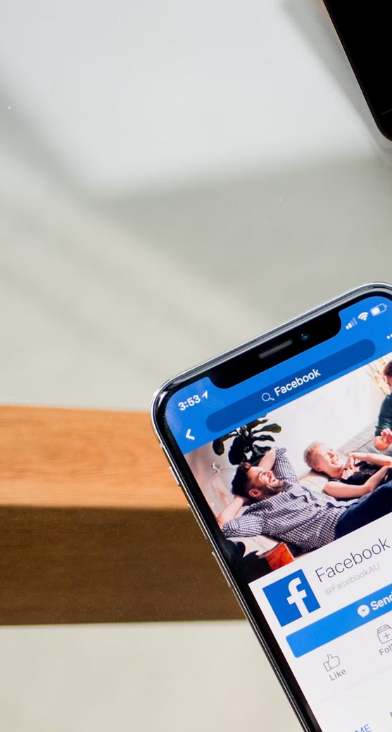 A smartphone showing a Facebook page beside a laptop on a wooden desk