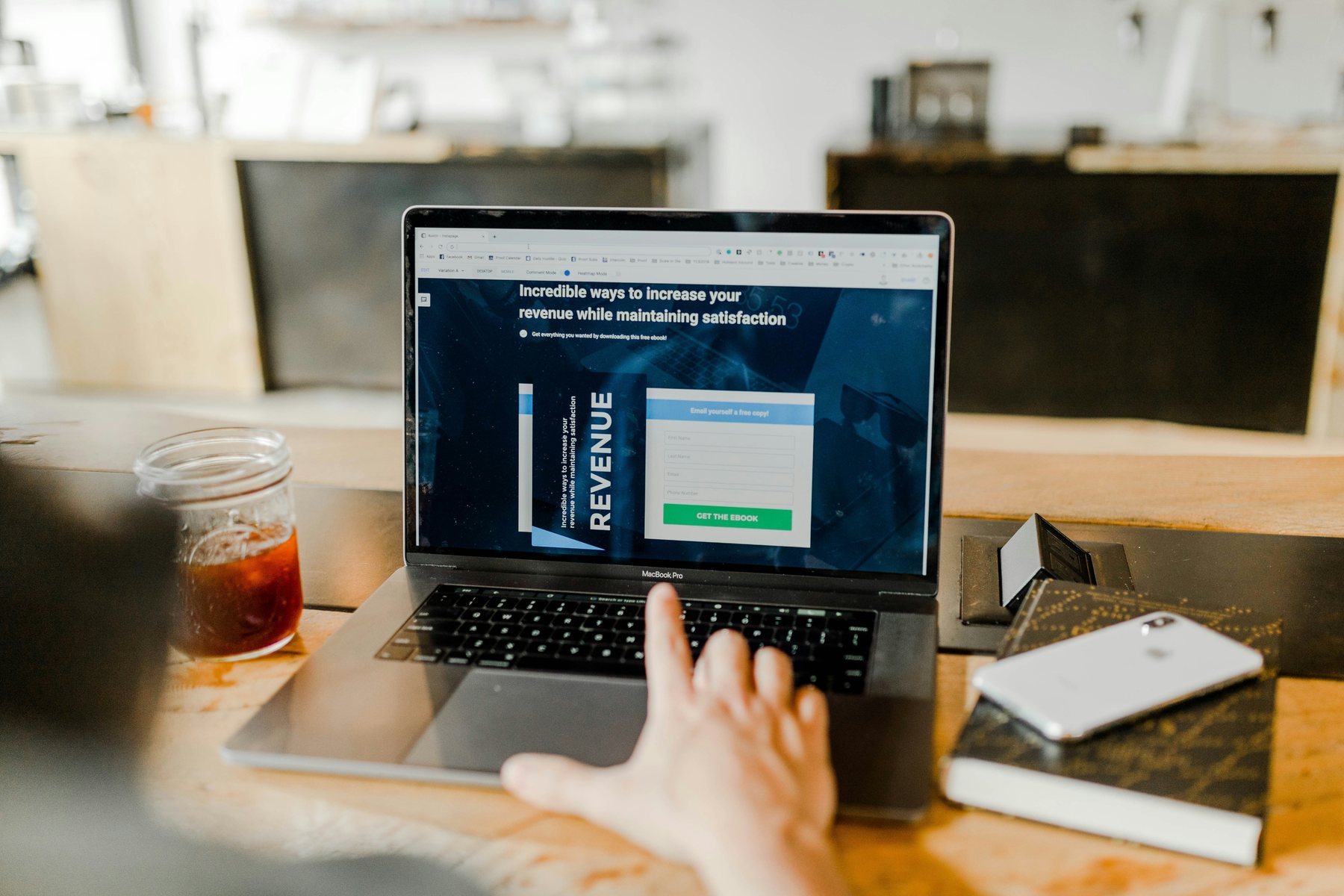 Laptop screen displaying a landing page, on a wooden desk beside a cold-brew coffee and phone